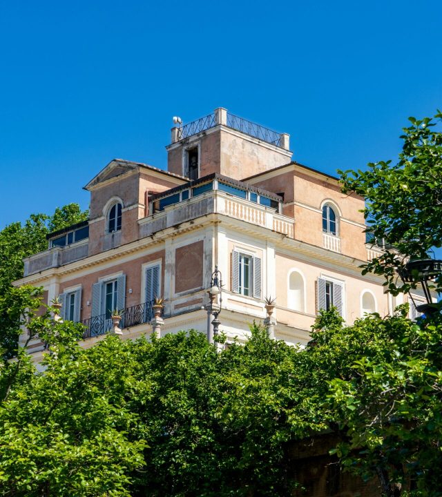 A stunning villa nestled among vibrant trees under a clear blue sky in Rome, Italy.